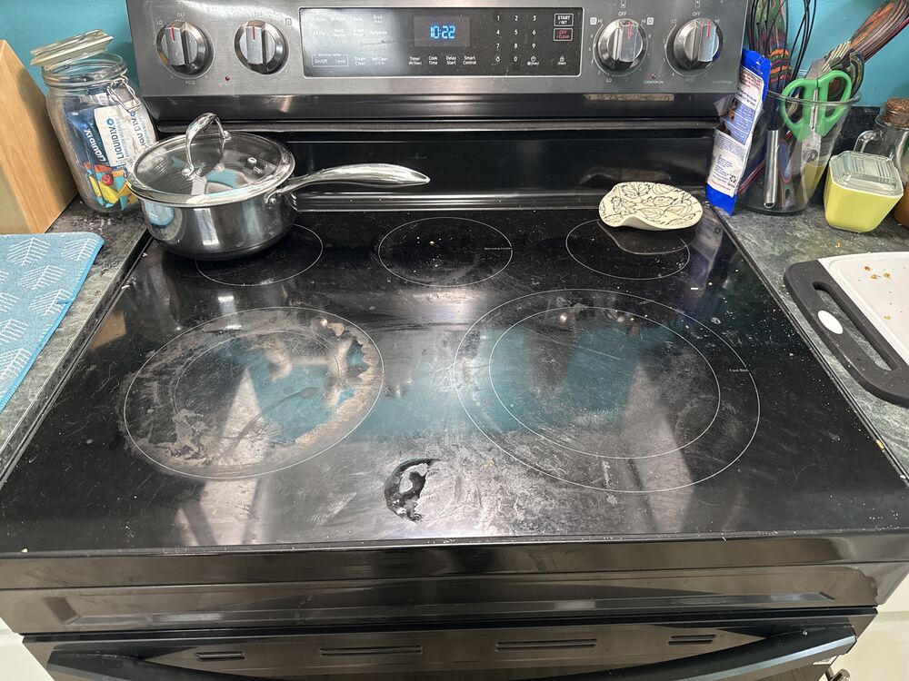 A glass stovetop with cooked-on residue and smudges before cleaning.